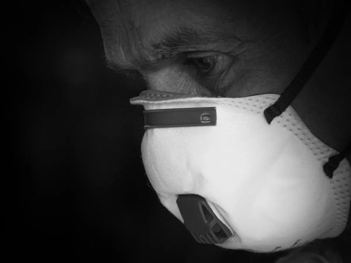 A close-up of a person wearing a white respirator mask, their eyes looking down, with the focus on the mask and the person's eyes.